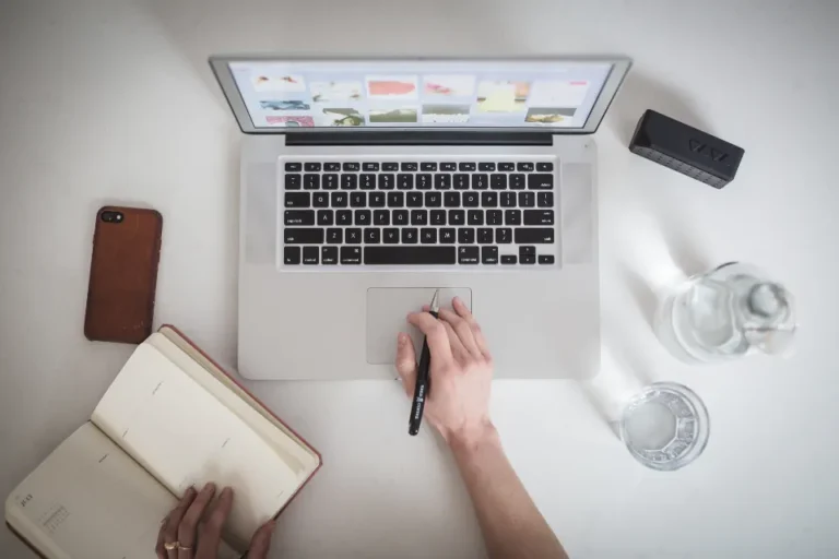 Hand working at a laptop beside an open notebook and phone