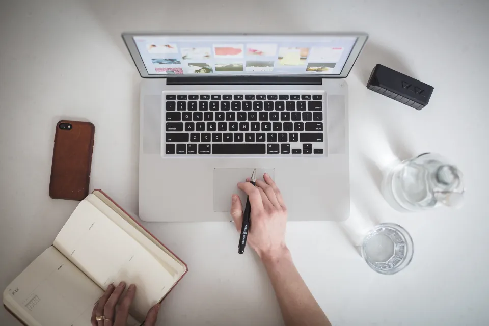 Hand working at a laptop beside an open notebook and phone