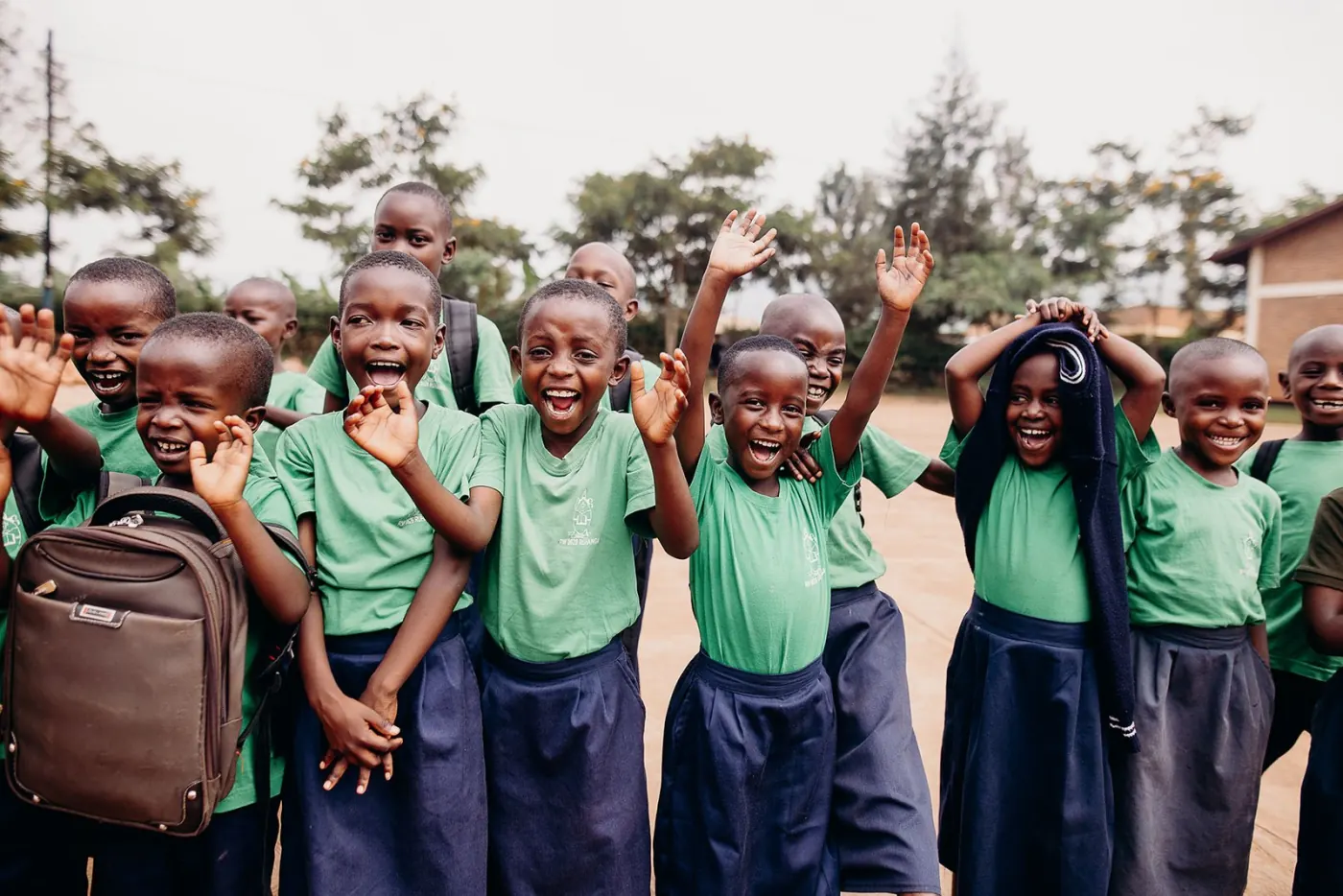 Children in school uniforms smiling and waving outside a Compassion International child development center.