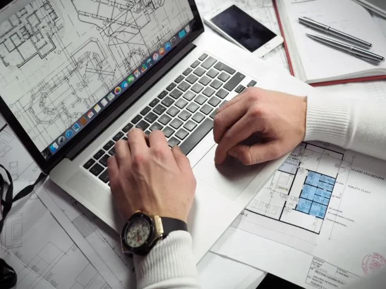 Hands working on a laptop over construction drawings and a floor plan