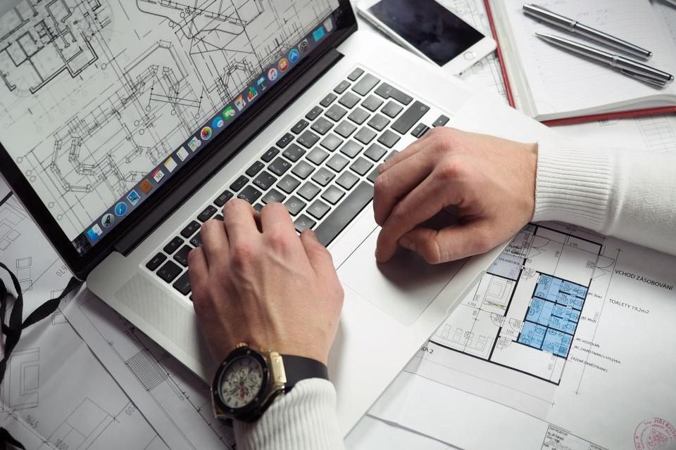 Laptop and notebook resting on construction blueprints during a takeoff