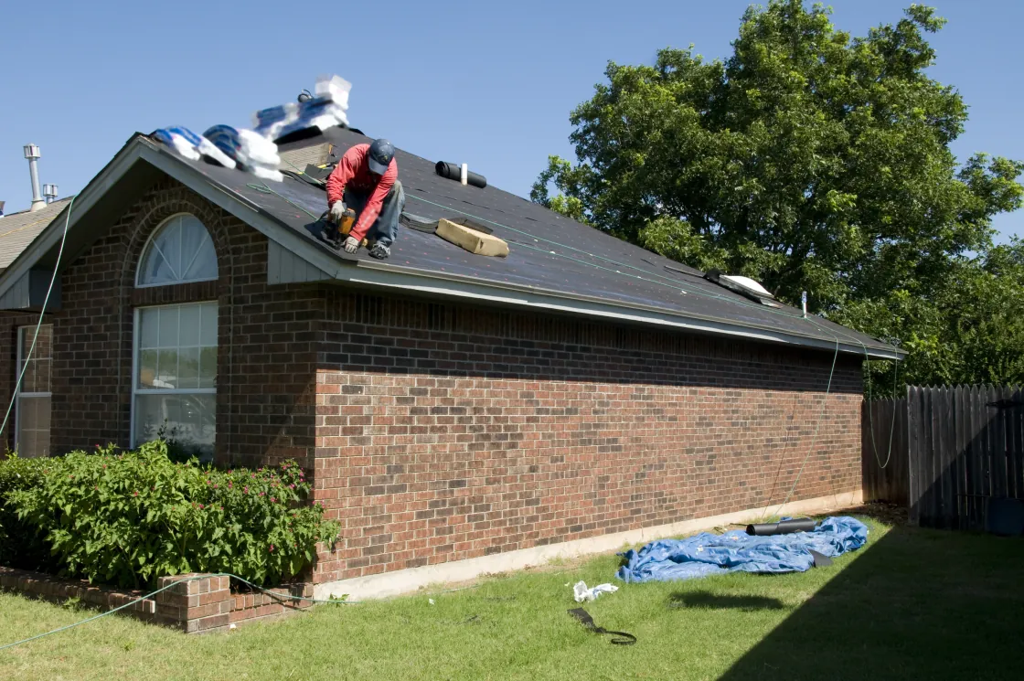 Roofer replacing a storm-damaged roof on a brick house